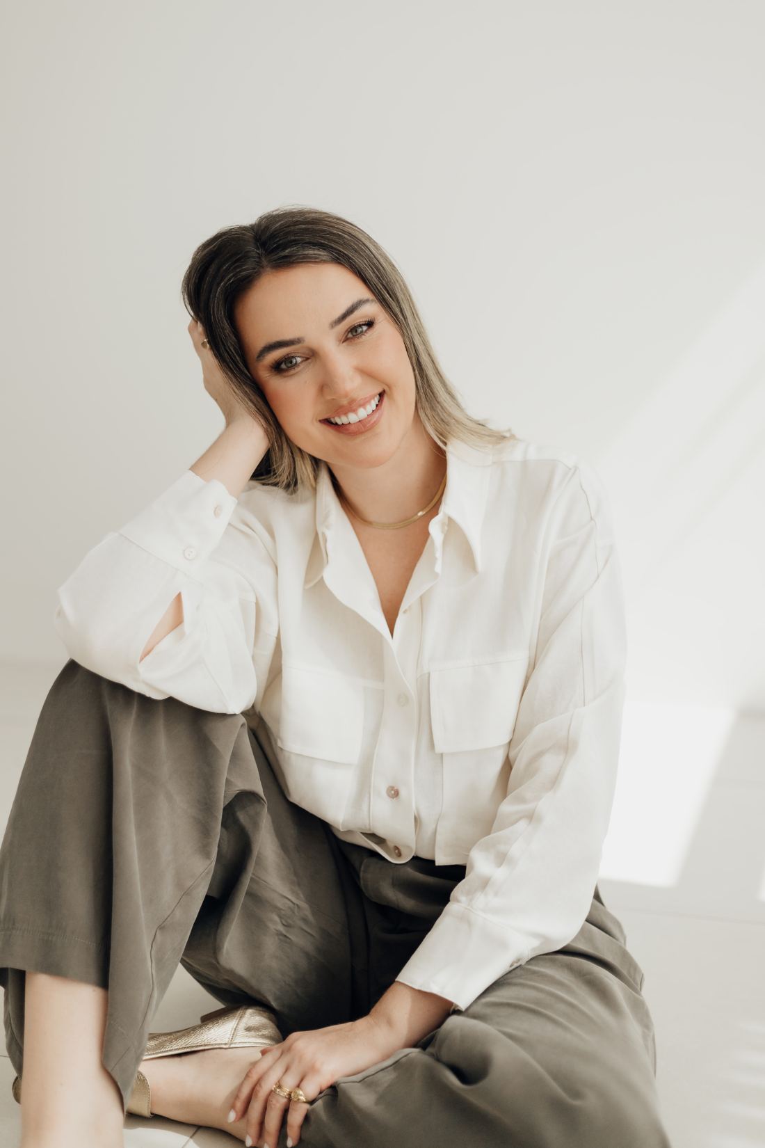 Daniela sentada no chão, sorrindo, em um ambiente claro