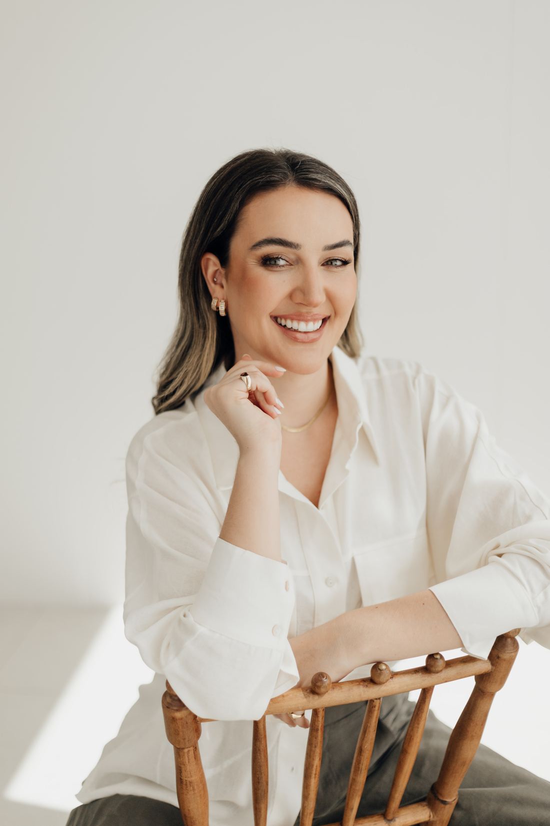 Daniela sentada de frente para o encosto de uma cadeira, sorrindo