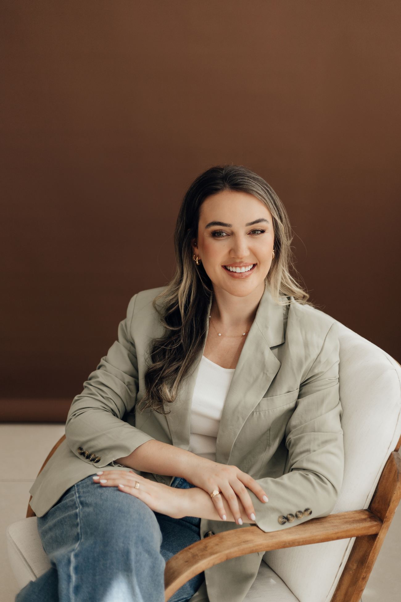 Daniela sentada em uma poltrona, de blazer verde, sorrindo